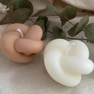 Duas velas decorativas em forma de nó sobre tecido bege claro