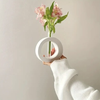 Vaso decorativo branco circular com flores cor-de-rosa e folhas verdes em fundo cinza