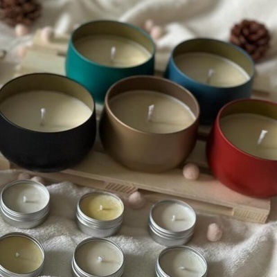 Velas em recipientes coloridos e pequenas velas em latas prateadas sobre tecido branco