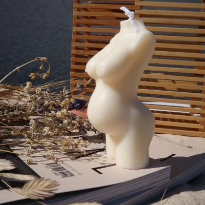 Vela decorativa formato torso feminino em cera branca com flores secas e mala de madeira ao fundo