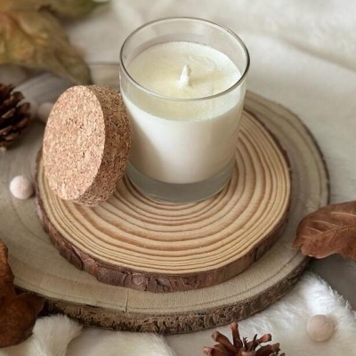 Vela branca em copo de vidro com tampa de cortiça sobre madeira e decoração de outono