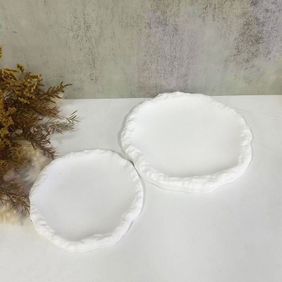 Dois pratos brancos cerâmicos com bordas onduladas sobre mesa branca e fundo cinzento