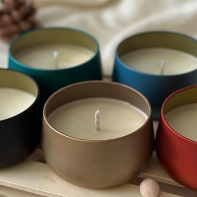 Cinco velas em copos metálicos coloridos sobre uma superfície clara