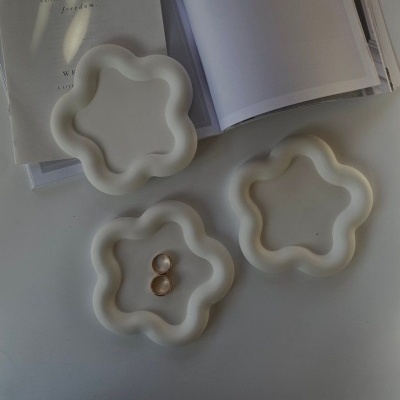 Três pratos brancos em forma de flor com brincos dourados e livros abertos ao fundo.