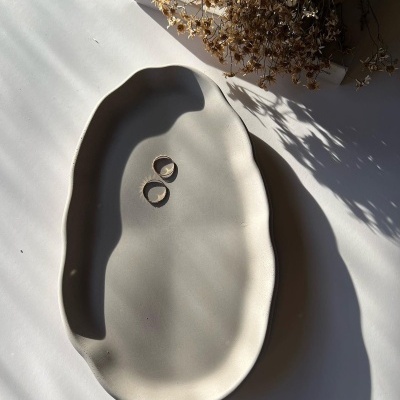 Prato cerâmico branco com argolas douradas e ramo seco sobre livro