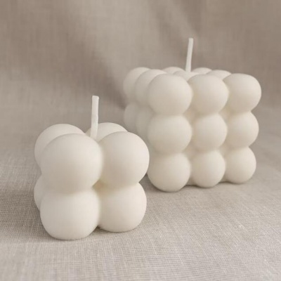 Duas velas brancas em forma de cubo com textura de bolas sobre superfície bege