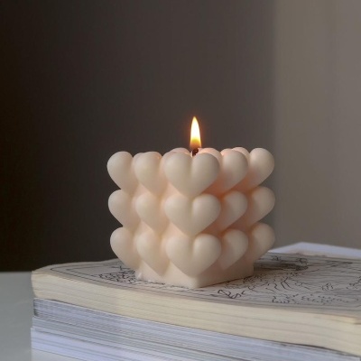 Vela branca em forma de cubo com corações acesa sobre livros