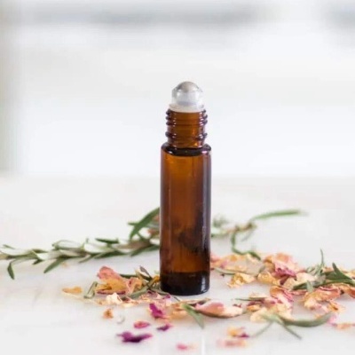 Frasco de vidro âmbar com dispensador roll-on rodeado por folhas e pétalas secas