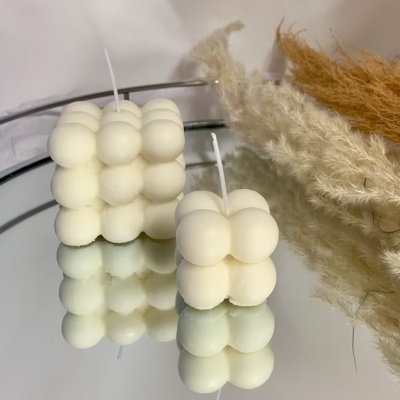 Velas em forma de cubos com bolhas em cima de superfície espelhada com plantas secas ao fundo