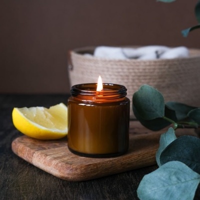 Vela em frasco de vidro castanho com limão e folhas verdes sobre tábua de madeira