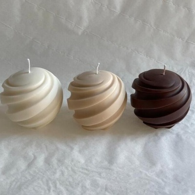 Três velas esféricas com padrão espiral em branco, bege e castanho sobre tecido branco