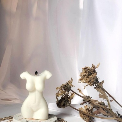 Vela branca forma torso feminino em suporte branco com colares e flores secas