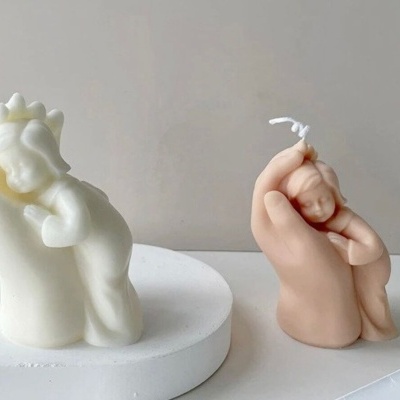 Duas velas decorativas, uma branca com criança e dinossauro, outra rosa com mão a segurar bebé