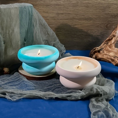 Dois castiçais de vela azul claro e branco sobre tecidos cinza e azul com fundo de madeira