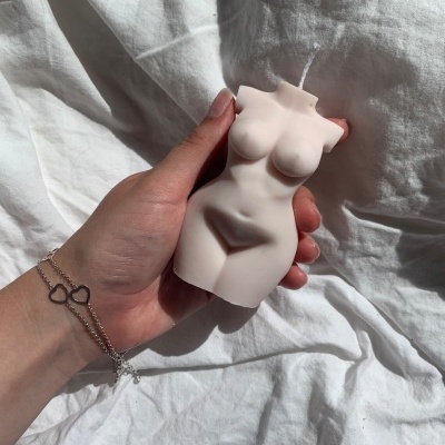 Vela decorativa em forma de torso feminino em mão com fundo de tecido branco