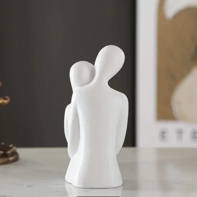 Escultura abstrata branca de duas pessoas em cerâmica sobre superfície branca.