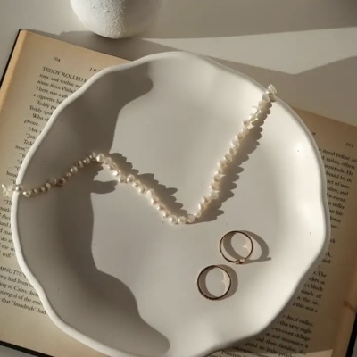 Colar de pérolas e dois anéis dourados numa tigela branca sobre um livro aberto