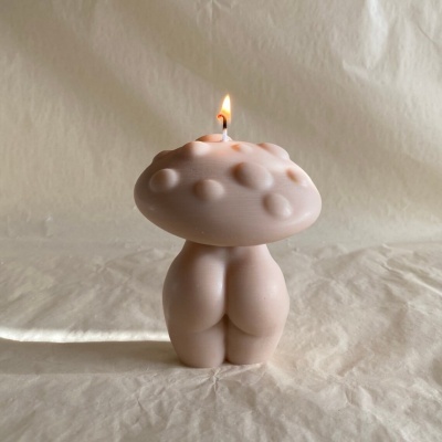 Vela rosa clara em forma de cogumelo com textura, acesa sobre tecido bege