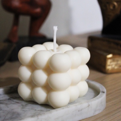 Vela branca em forma de cubo de bolhas numa base de mármore com fundo desfocado