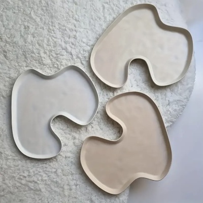 Três pratos irregulares em tons neutros sobre tecido branco felpudo