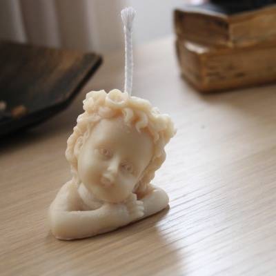 Vela decorativa em forma de anjo creme sobre mesa de madeira