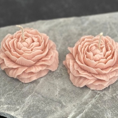 Duas velas rosa em forma de flores colocadas numa superfície de pedra cinzenta
