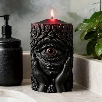 Vela preta decorativa com padrão detalhado e rosto com olho no centro acesa numa bancada de mármore