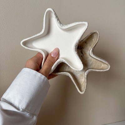 Dois organizadores em forma de estrela, um branco e outro bege, segurados por uma mão contra uma parede bege.