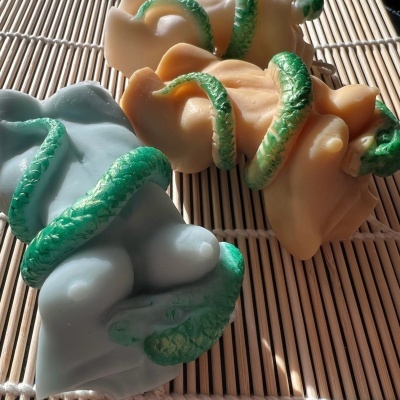 Três velas decorativas com cobras verdes sobre tapete de bambu