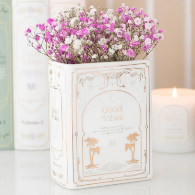 Vaso cerâmico branco decorado com flores cor-de-rosa e brancas e vela acesa ao fundo