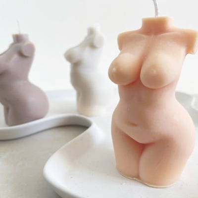 Vela decorativa em forma de corpo feminino em tons de bege e branco.
