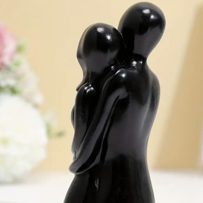 Escultura abstrata de casal em abraço, preta e brilhante, com fundo de flores e parede clara