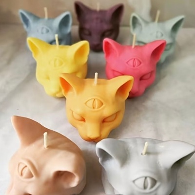 Velas coloridas em forma de cabeça de gato com um terceiro olho.
