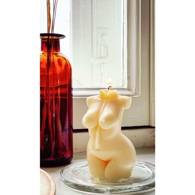 Vela decorativa em forma de corpo feminino creme numa janela ao lado de difusor em vidro âmbar