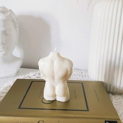 Vela de torso humano branca sobre livro Gucci com busto e vaso branco ao redor