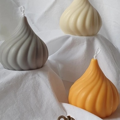 Três velas onduladas em cinza, branco e amarelo com um par de brincos dourados sobre tecido branco