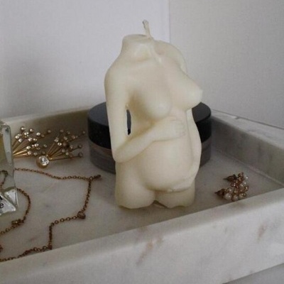 Vela em forma de corpo feminino grávido numa bandeja de mármore com joias e perfume
