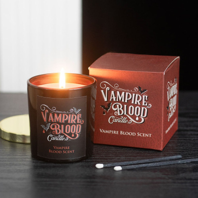 Vela Vampire Blood acesa com caixa e palhinhas pretas ao lado sobre mesa preta