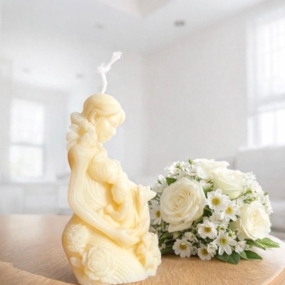 Vela decorativa em forma de mãe e criança com flores ao lado em mesa de madeira