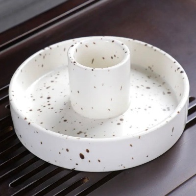 Suporte de cerâmica branco com manchas castanhas e suporte cilíndrico central sobre superfície de madeira escura