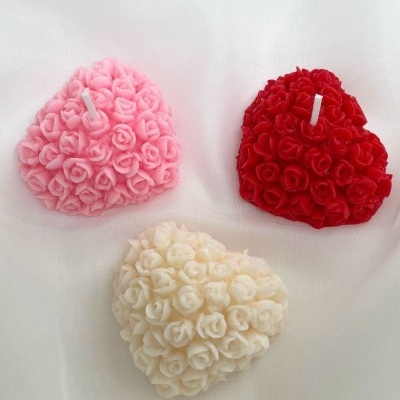 Três velas em forma de coração decoradas com pequenas flores, em rosa, vermelho e branco.