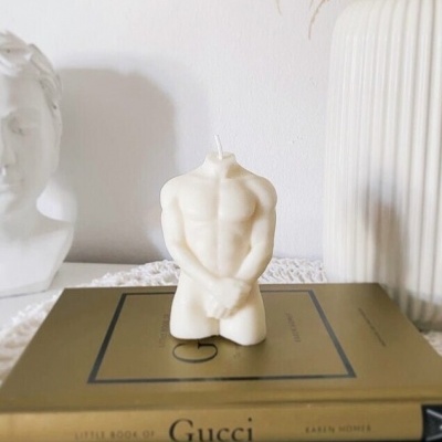 Vela em forma de torso masculino branco sobre livros de moda em ambiente interior