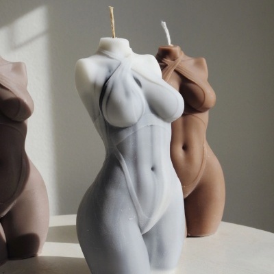 Velas corpo feminino esculpidas em cera, em branco e castanho, sobre superfície branca