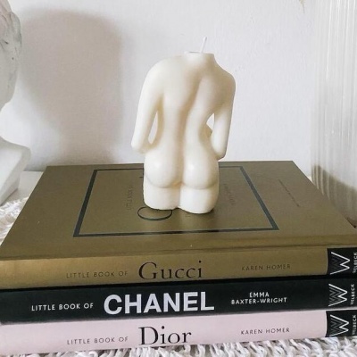 Vela branca em forma de corpo humano feminino sobre livros de moda Gucci, Chanel e Dior
