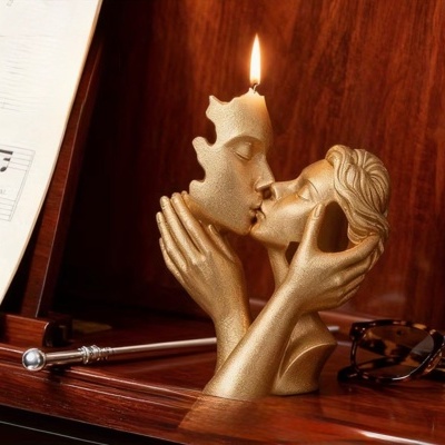 Escultura dourada de casal a beijar-se com vela acesa numa cabeça, sobre madeira com partitura e óculos