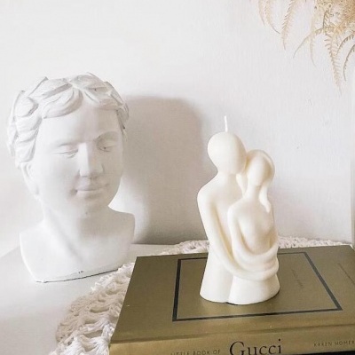 Cabeça decorativa branca e vela em forma de casal abraçado sobre livros e toalha branca rendada