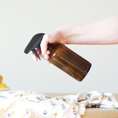 Garrafa de spray de vidro castanho com tampa preta e tecido com padrão floral em cima de mesa