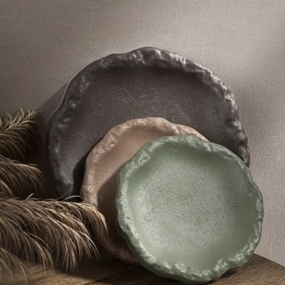 Três pratos decorativos de cerâmica com bordas onduladas em cinza, bege e verde claro