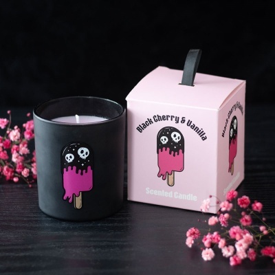Vela numa jarra preta ao lado de caixa rosa com design de gelado e texto sobre aroma