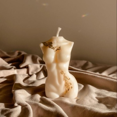 Vela decorativa em forma de torso feminino creme com detalhes dourados sobre tecido bege